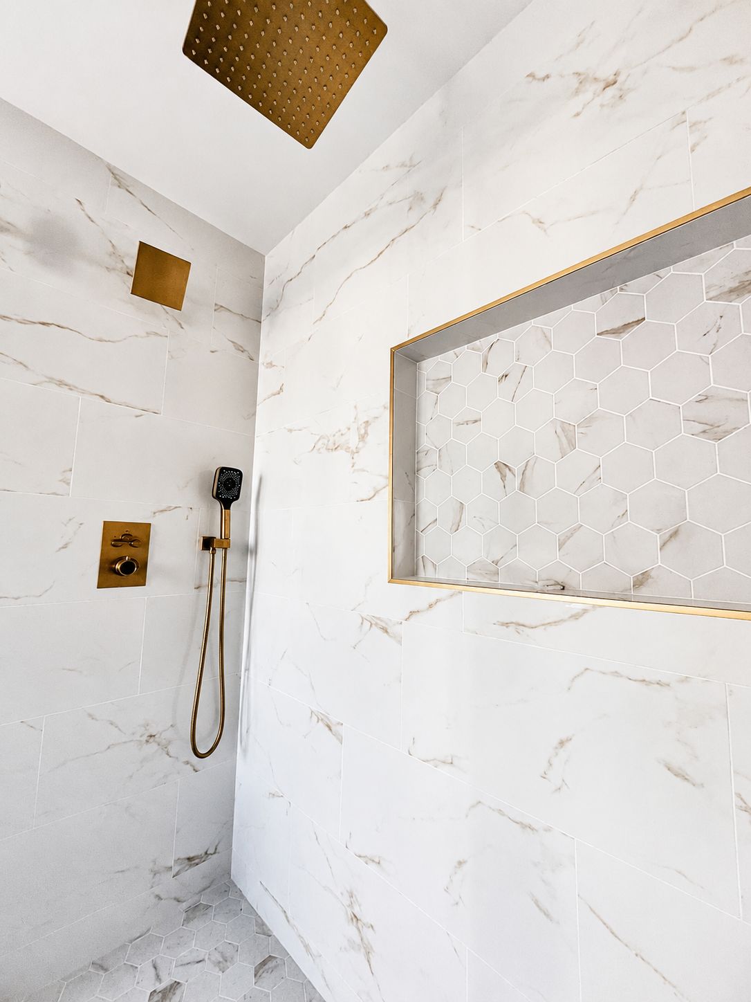 Marble shower detail with brushed gold fixtures and hexagon tile niche
